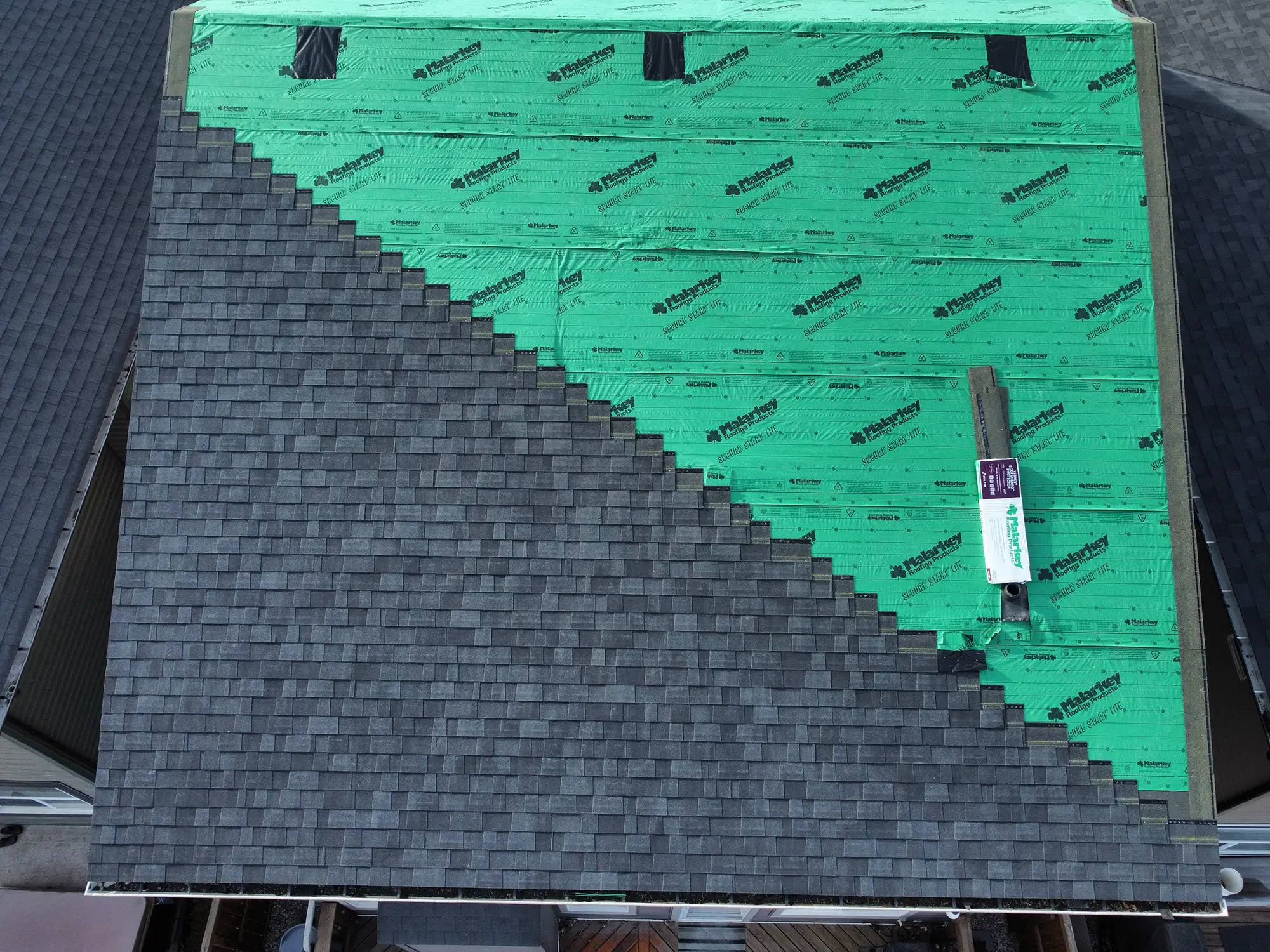 Aerial view of asphalt shingles being installed over synthetic underlayment during a roof replacement on a Calgary home